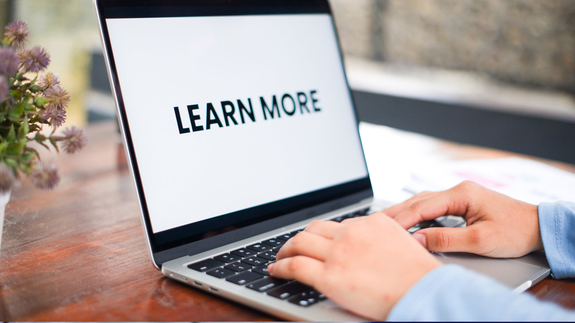Hands typing on a laptop with the bold text LEARN MORE displayed on the screen